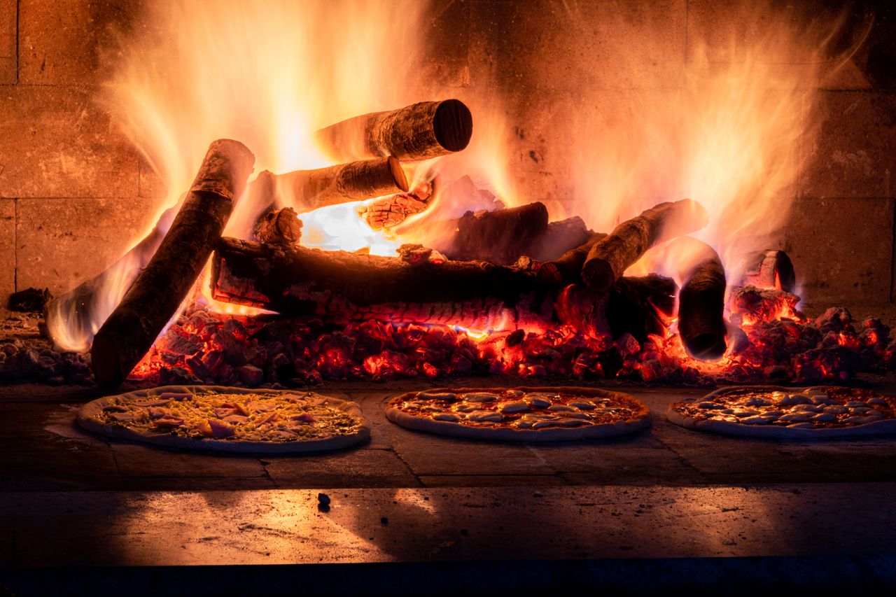 heros-img Rustic wood-fired pizza oven with flames and pizzas baking, capturing the warmth of traditional cooking.