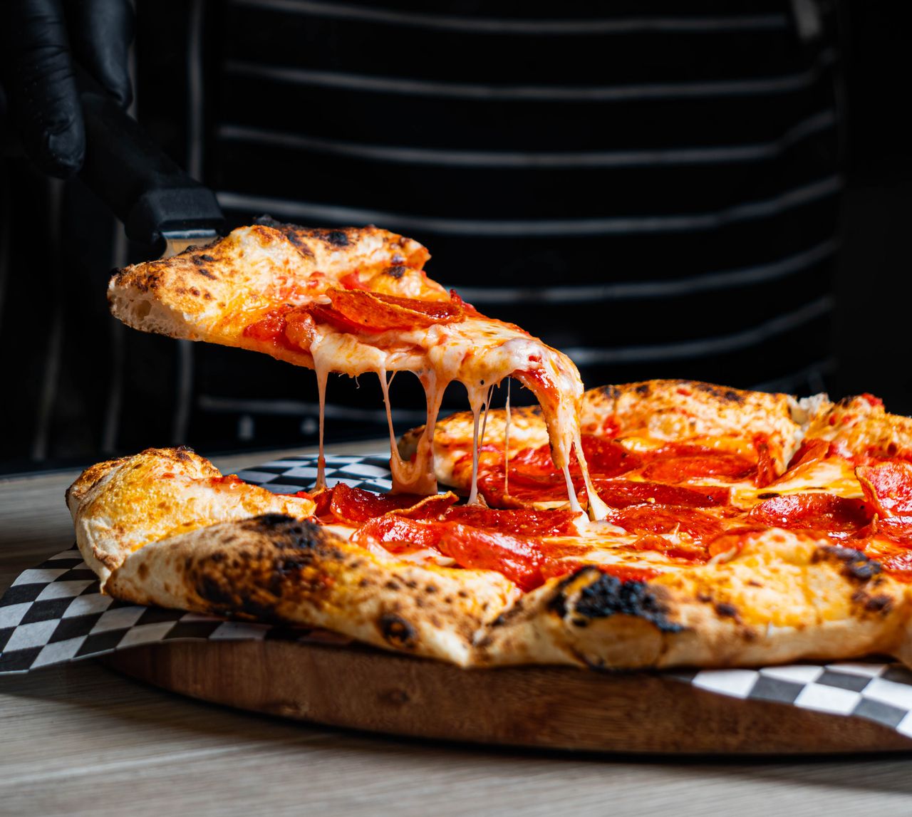 Close-up of a cheese-laden pepperoni pizza with a slice being served, ideal for food enthusiasts.