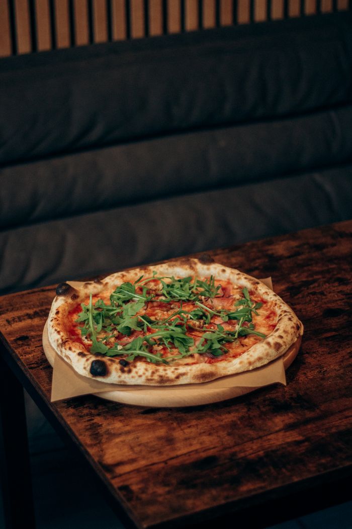 services-02 A freshly baked wood-fired pizza topped with arugula served on a rustic wooden table.