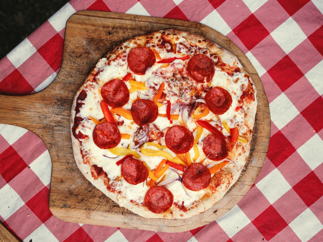 Top view of a delicious pepperoni pizza photographed outdoors on a checkered tablecloth.