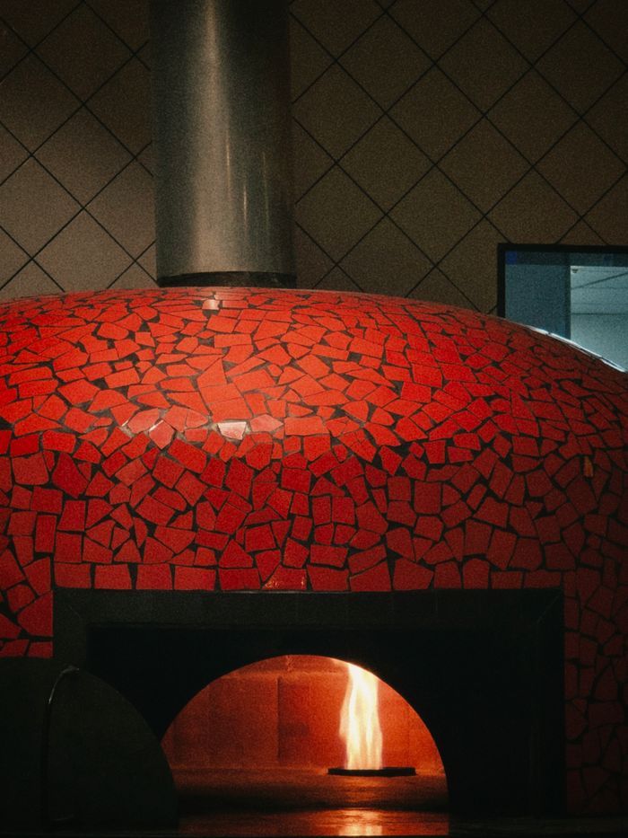 services-01 A traditional wood-fired pizza oven adorned with a vibrant red tile mosaic and a glowing flame inside.