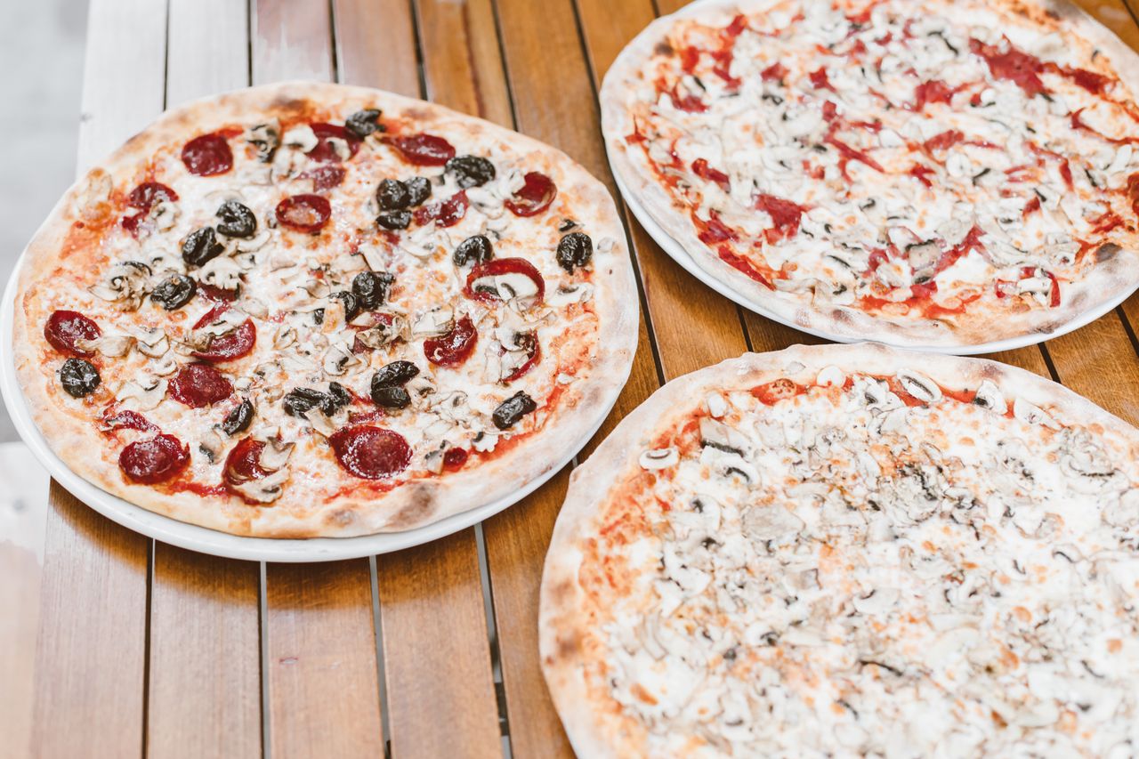 services-04 Close-up of assorted pizzas with mushrooms, pepperoni, and olives on a wooden table.